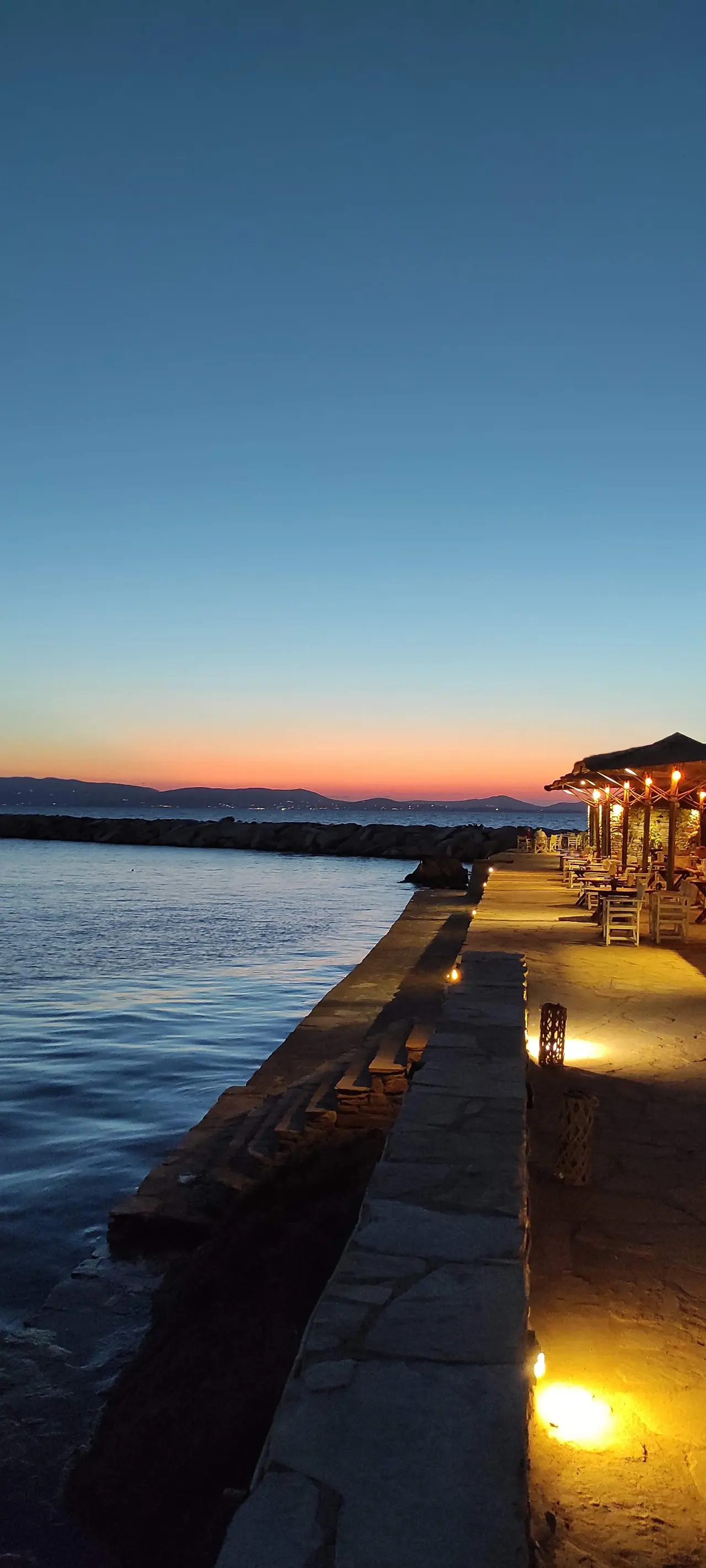 A lit stone quay and taverna at dusk